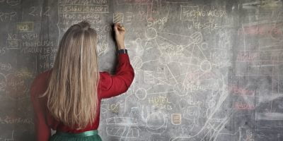 woman in red long sleeve writing on chalk board